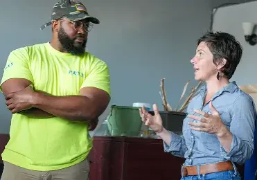 St. Louis Mayor Cara Spencer gestures while speaking with a man in a neon yellow shirt and camouflage hat.